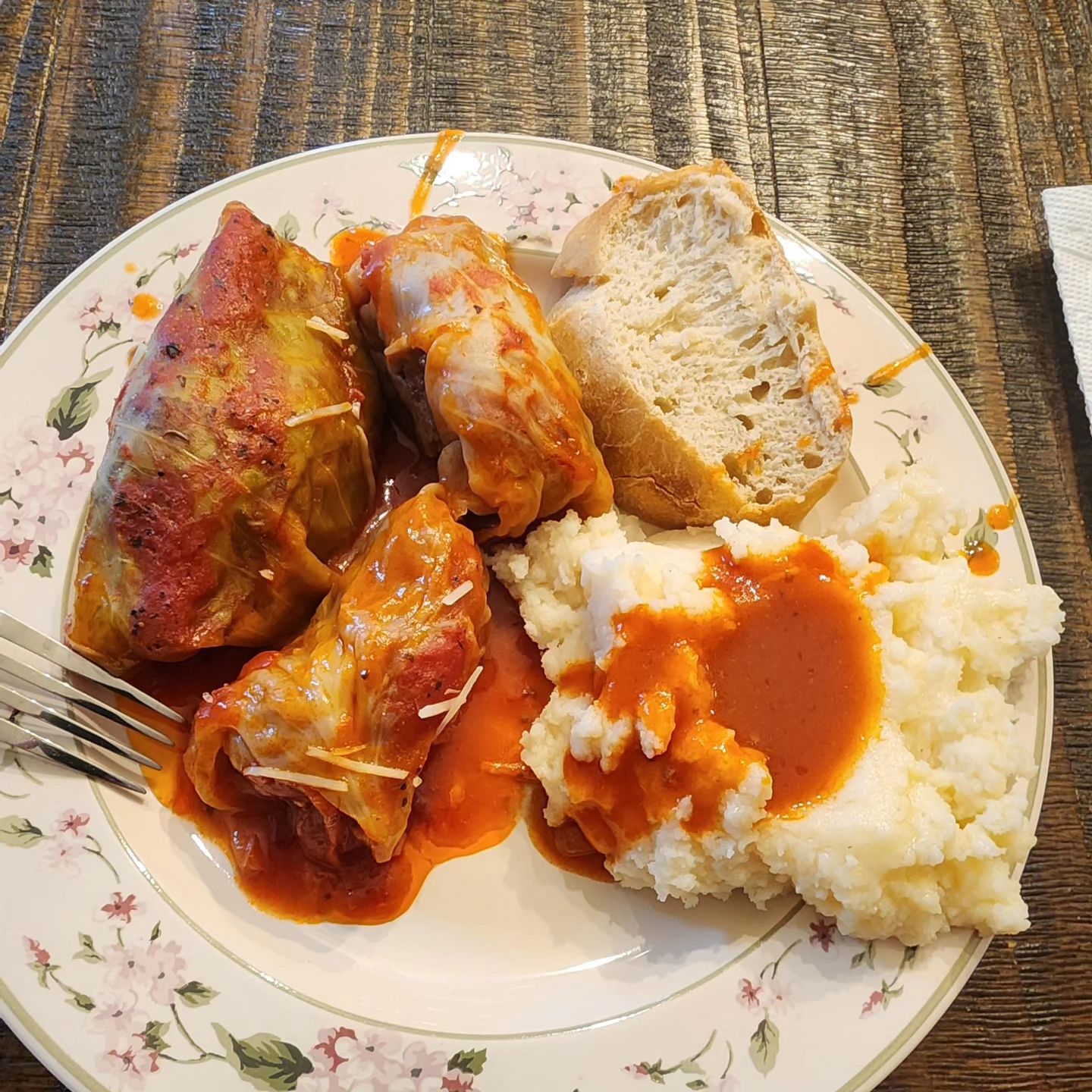 3 stuffed cabbage rolls & mashed potatoes on a plate, with a side of bread.