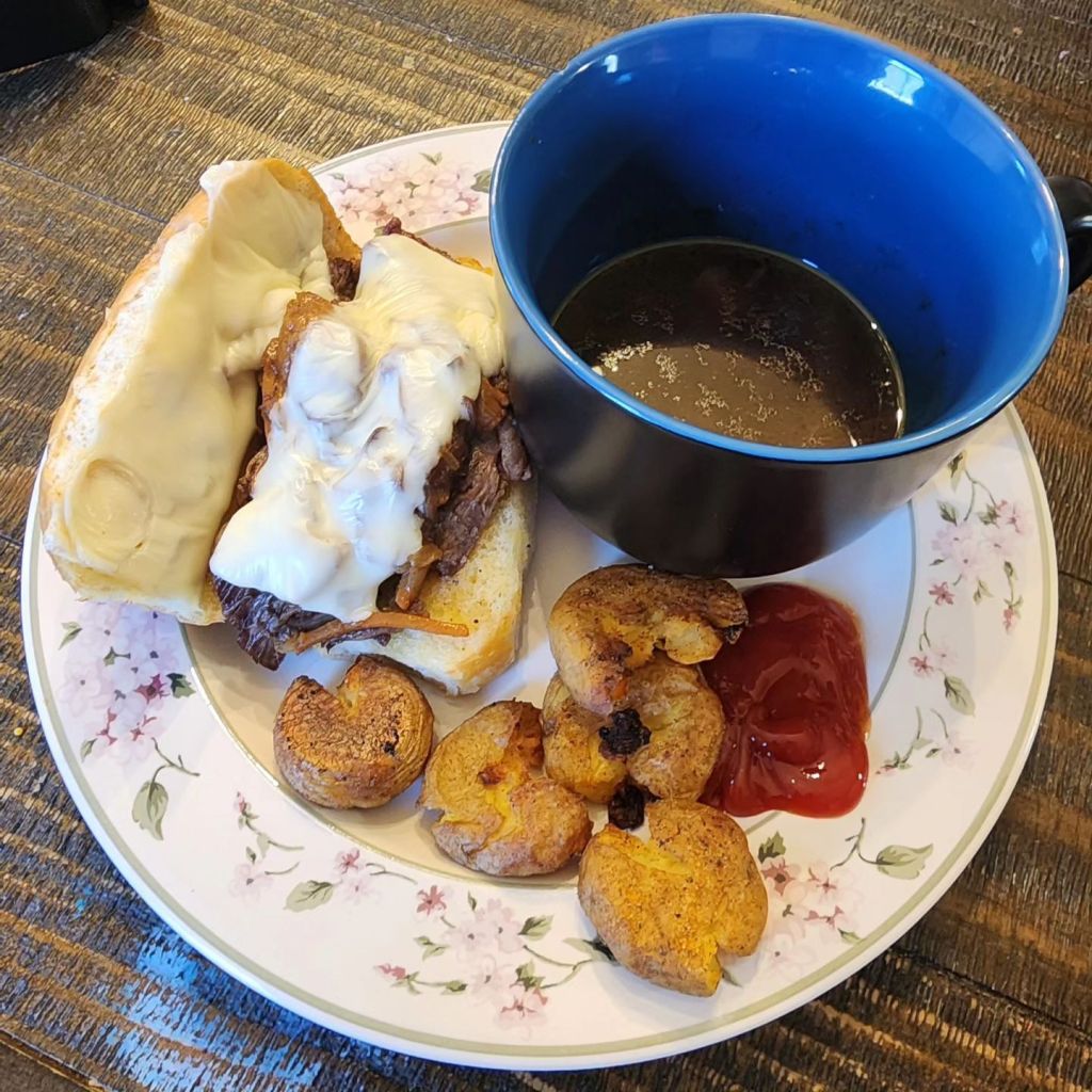 A French Dip sandwich with some Au Jus and smashed potatoes.